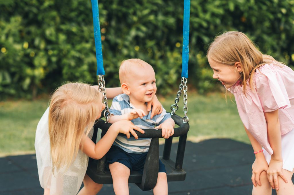 Family of 3 kids playing together outside, big sisters taking care of baby brother