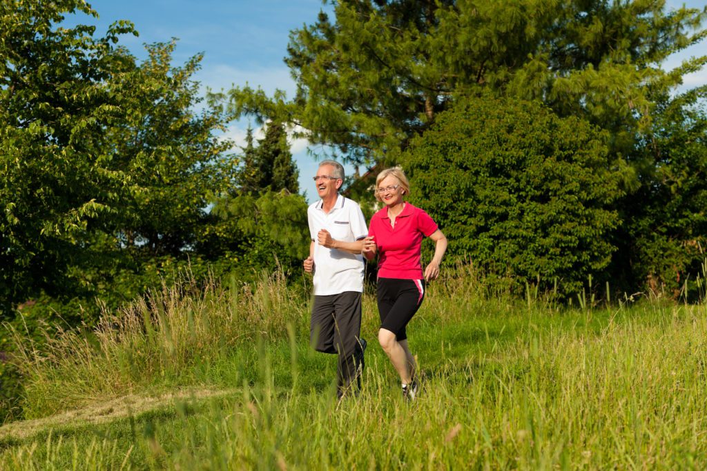 Mature or senior couple doing sport outdoors, jogging down a path in summer