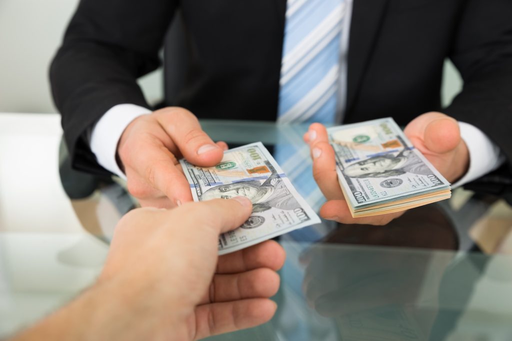 Cropped image of businessman passing money to colleague at table