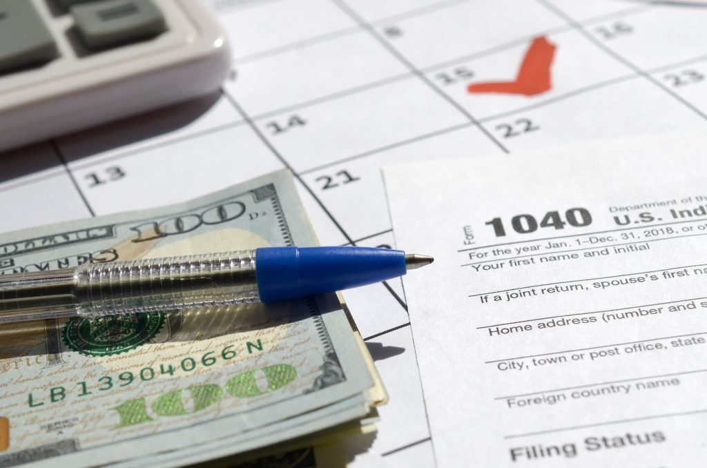 1040 Individual Income Tax Return blank with dollar bills, calculator and pen on calendar page with marked 15th April. Tax period concept. IRS Internal Revenue Service