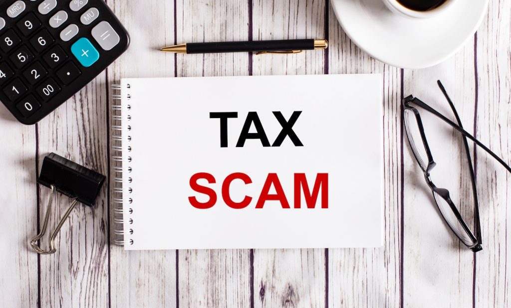 TAX SCAM is written in a white notepad near a calculator, coffee, glasses and a pen. Business concept