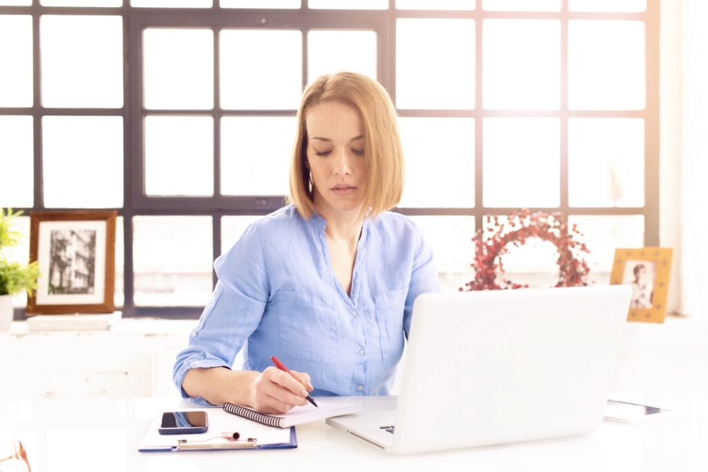 Shot of businesswoman doing some paperwork while sitting behind her notebook at office desk.