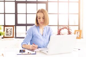 Shot of businesswoman doing some paperwork while sitting behind her notebook at office desk.