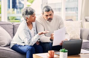 Old couple, laptop and discussion about retirement paperwork, life insurance and finance investment at home. People do taxes online, pension policy documents and budget, woman and man with bills.