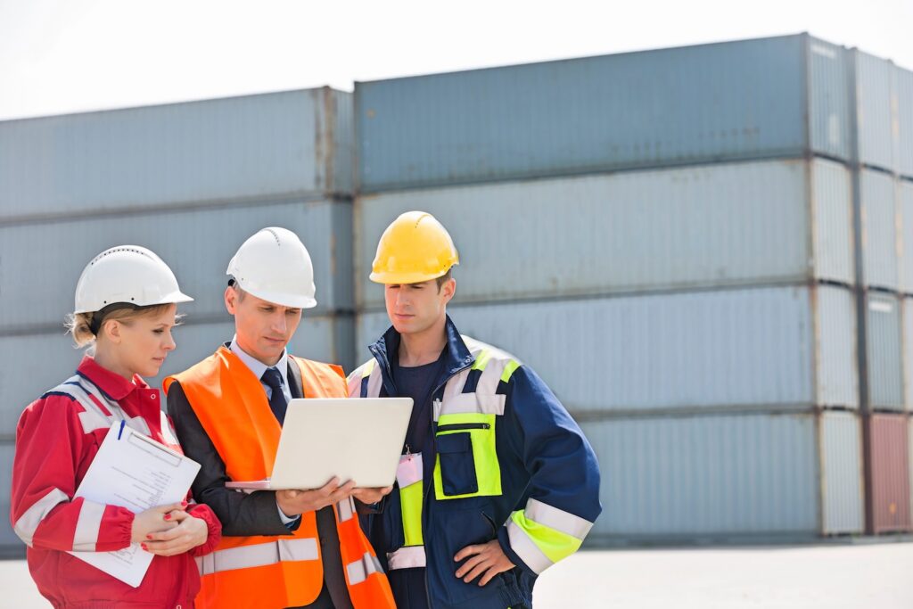 Workers discussing over laptop in shipping yard