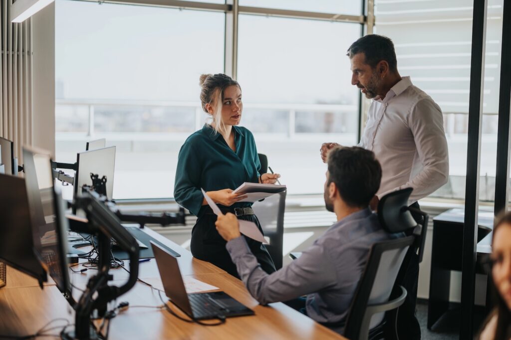 Business people gathered around a desk in a modern office, discussing documents. The atmosphere is professional, emphasizing teamwork and collaboration among business workers.